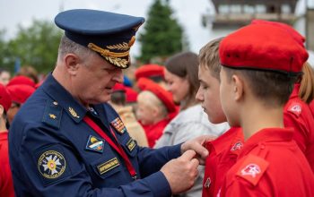 A Russian officer in uniform pinning a badge on a young recruit during an outdoor military ceremony.